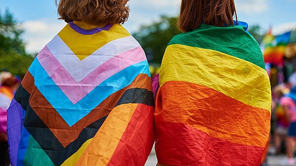 Two people wearing pride flags as a cape